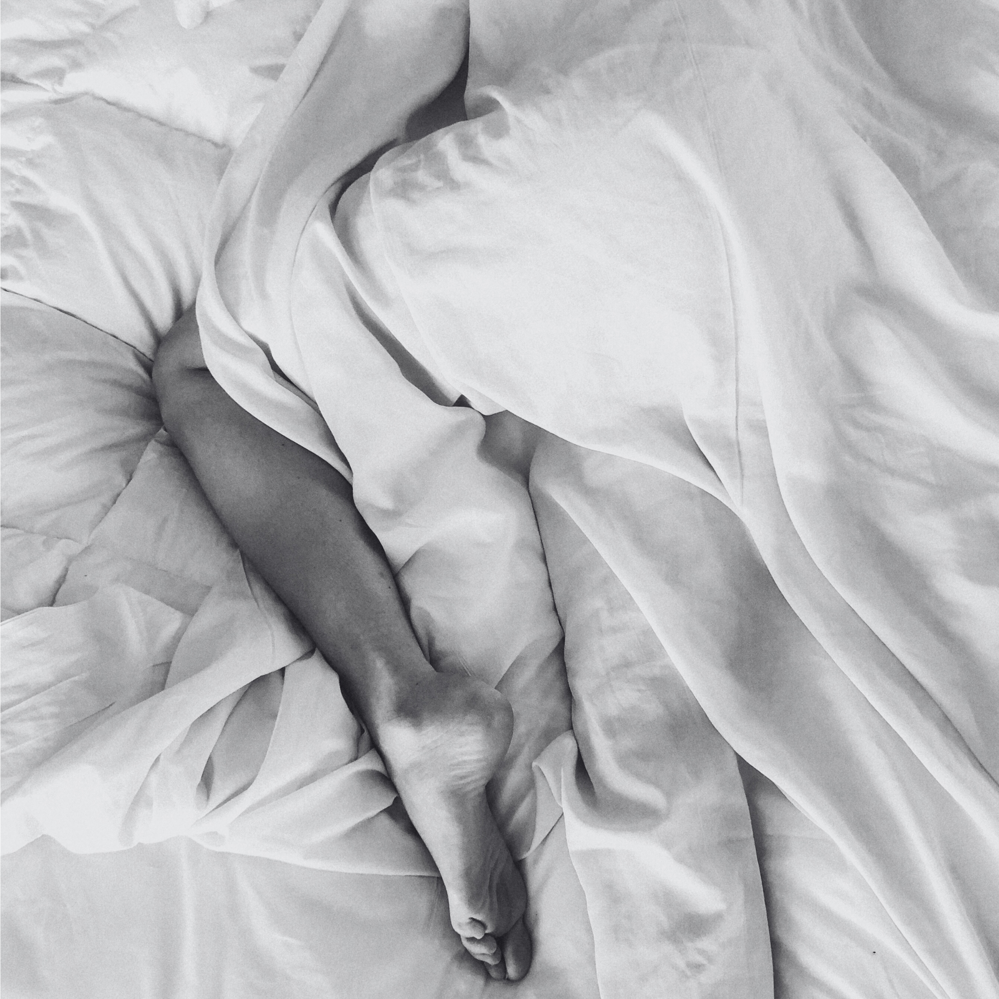 Close-up of a person's legs under white bedding