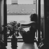 Person sitting by a window with a potted plant, looking out.