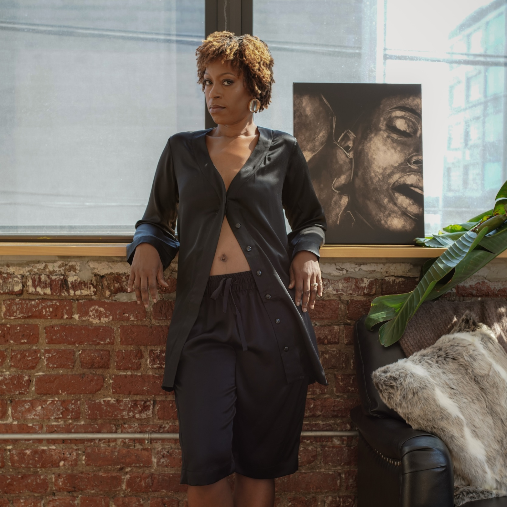 model wearing a je mérite, i deserve loungewear standing in front of a brick wall with a painting in the background