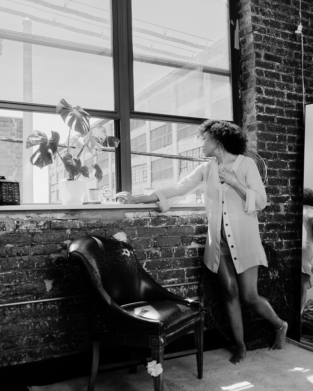 Woman standing by a window in a room with brick walls and a chair.