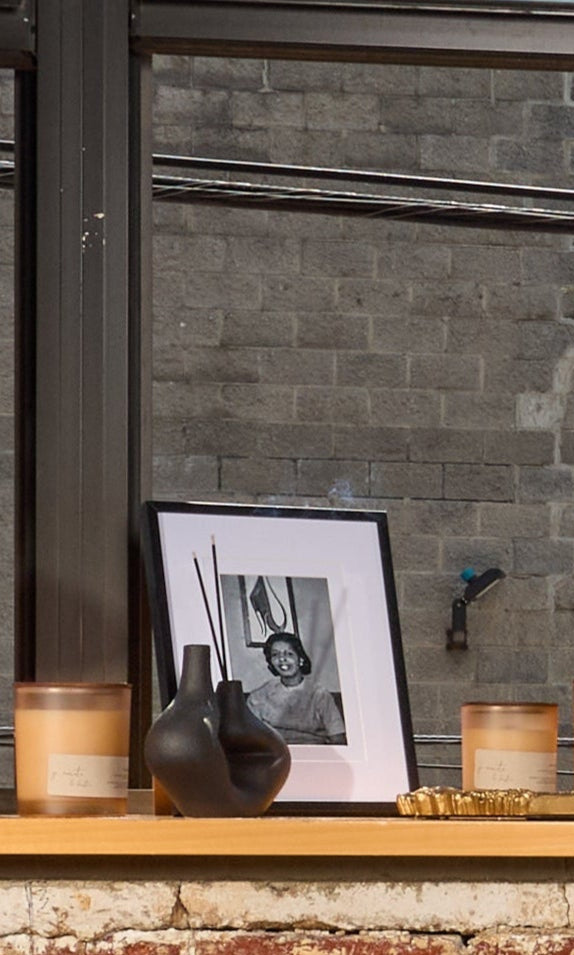 Woman sitting on a stool by a window in a room with brick walls and plants.
