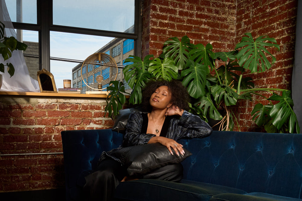 Woman sitting on a blue couch in a room with brick walls and plants