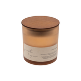 A jar candle with amber-colored wax in a translucent glass container, featuring a round wooden lid and a beige paper label with handwritten-style text, shown on a plain white background.
