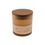 A soy wax candle in a clear amber glass jar with a round wooden lid and a beige paper label, shown on a plain white background.