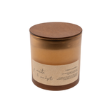 A soy wax candle in a clear amber glass jar with a round wooden lid and a beige paper label, shown on a plain white background.