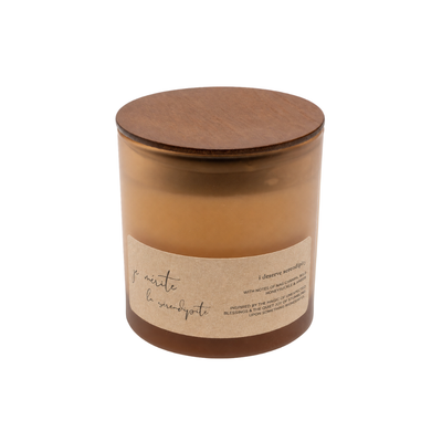 A soy wax candle in a clear amber glass jar with a round wooden lid and a beige paper label, shown on a plain white background.