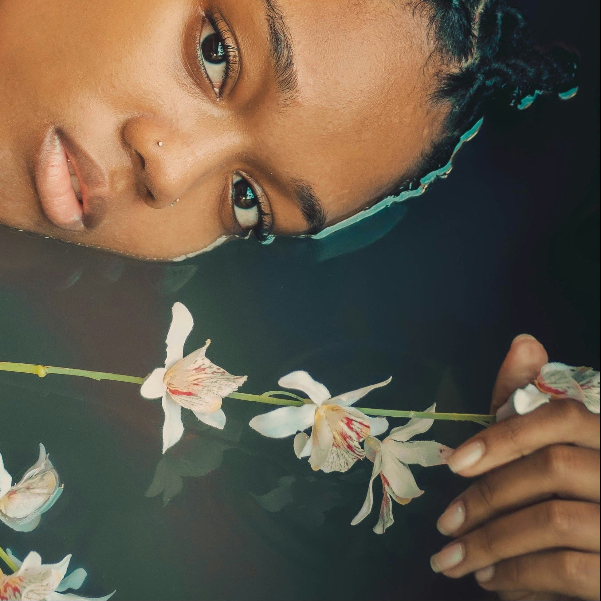 Woman holding a branch with flowers underwater, surrounded by greenery