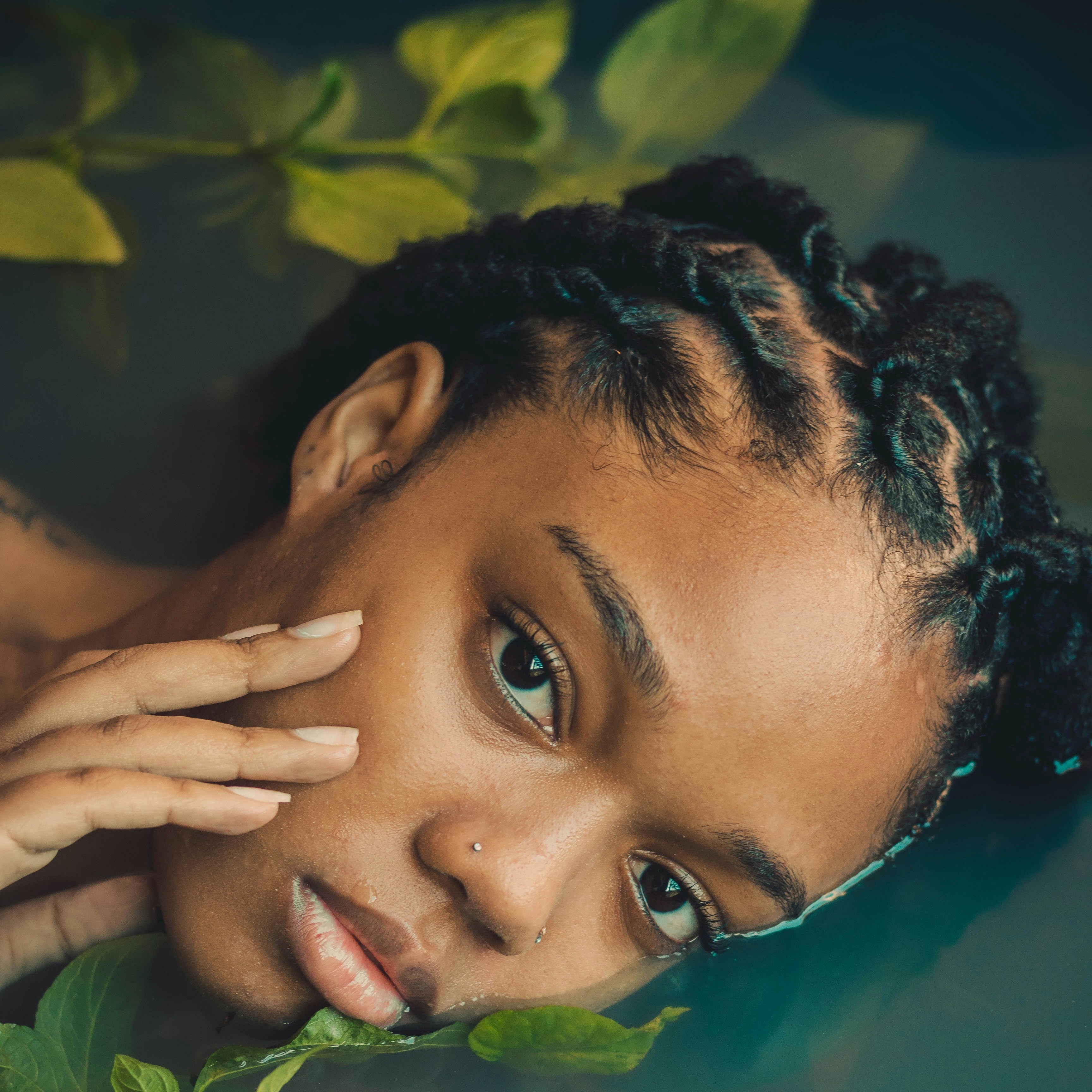 Woman with braided hair peeking through green leaves