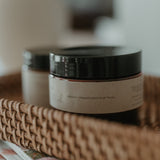 Jar of body butter on a woven tray with a blurred background