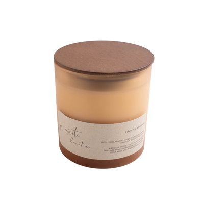 A soy wax candle in a clear glass jar with a brown wooden lid and a beige paper label, shown on a plain white background.