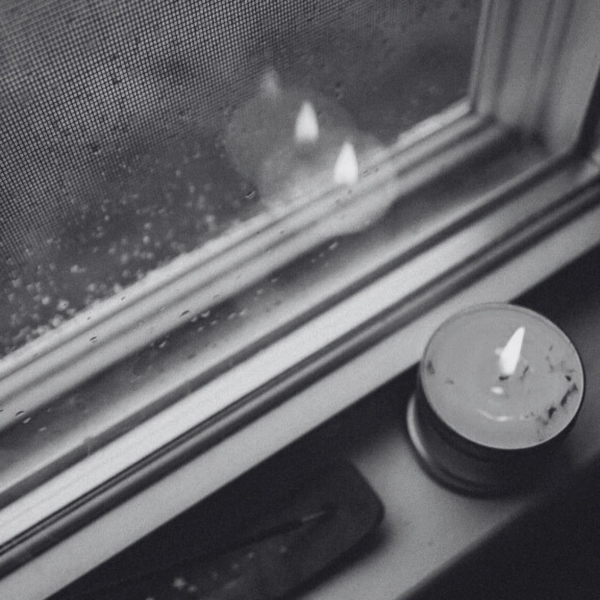 Candle on a windowsill with raindrops on the glass
