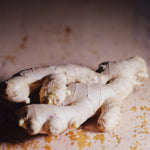 Fresh ginger root pieces with visible buds, resting on a rustic, weathered wooden surface with warm, dim lighting.