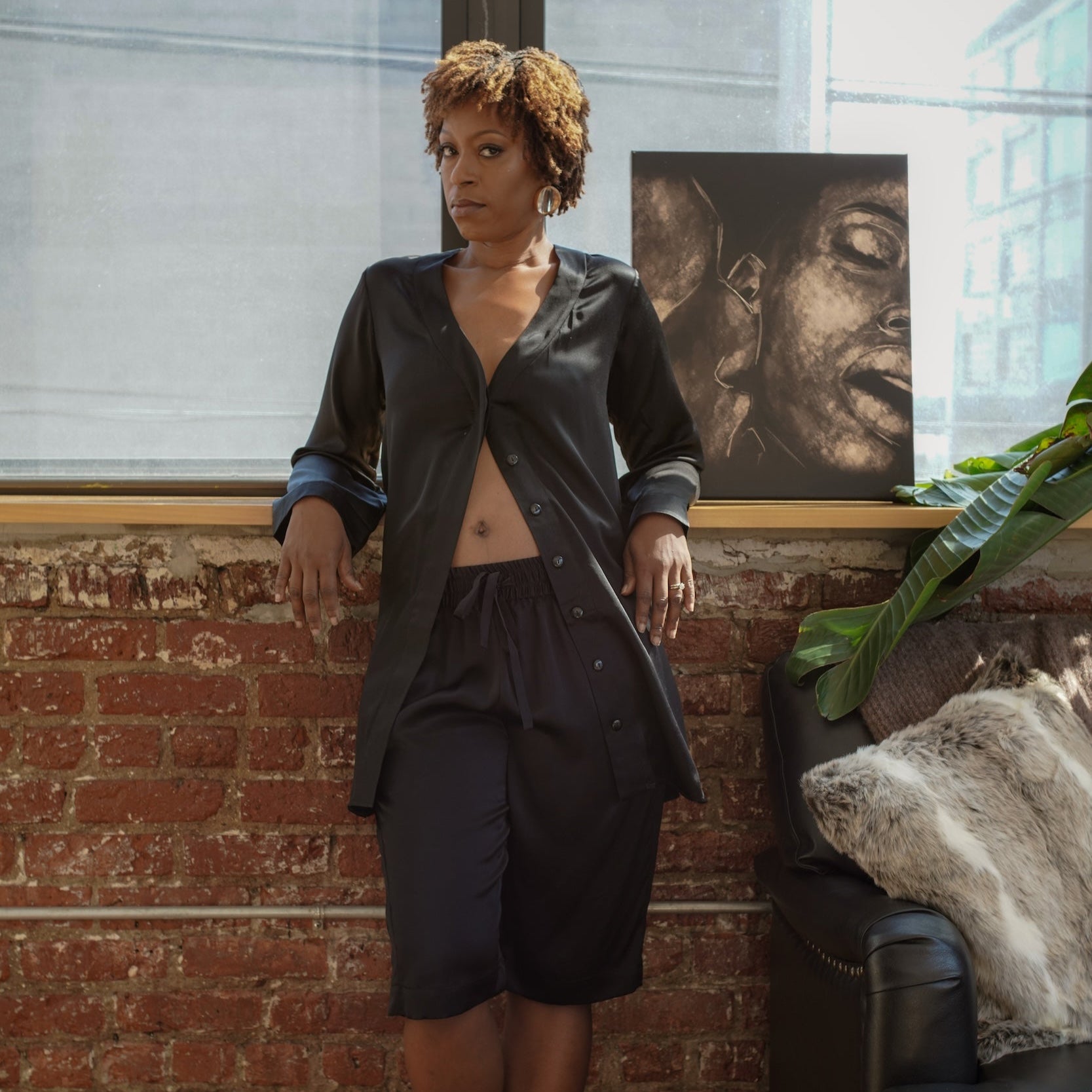 A woman standing in a room with a brick wall and a painting in the background, wearing a black silk tuxedo bermuda short with a drawstring design

made in the softest washed silk charmeuse, this bermuda short has an elastic waistband and drawstring closure  wear with a je mérite coordinating top or your favorite lingerie  wide elastic waist with drawstring closure sits at natural waist  sensual fit  washed 100% silk charmeuse  designed and made in new york city, new york - available in 0/2-20/22
