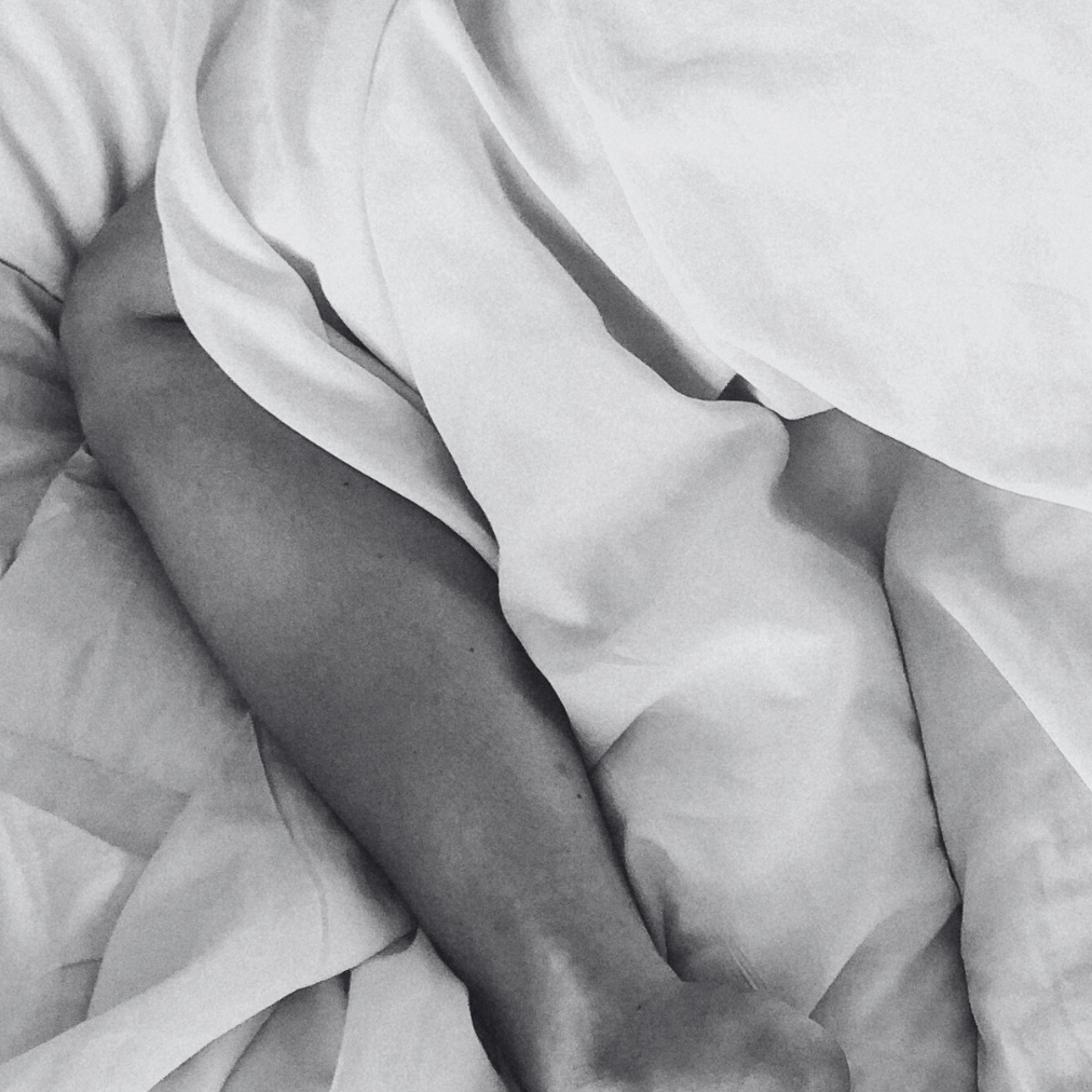 Close-up of a person's legs under white bedding