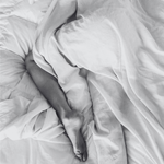 Close-up of a person's legs under white bedding