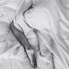Close-up of a person's legs under white bedding