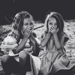 Two young girls sitting outdoors with their hands over their mouths.