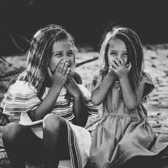 Two young girls sitting outdoors with their hands over their mouths.