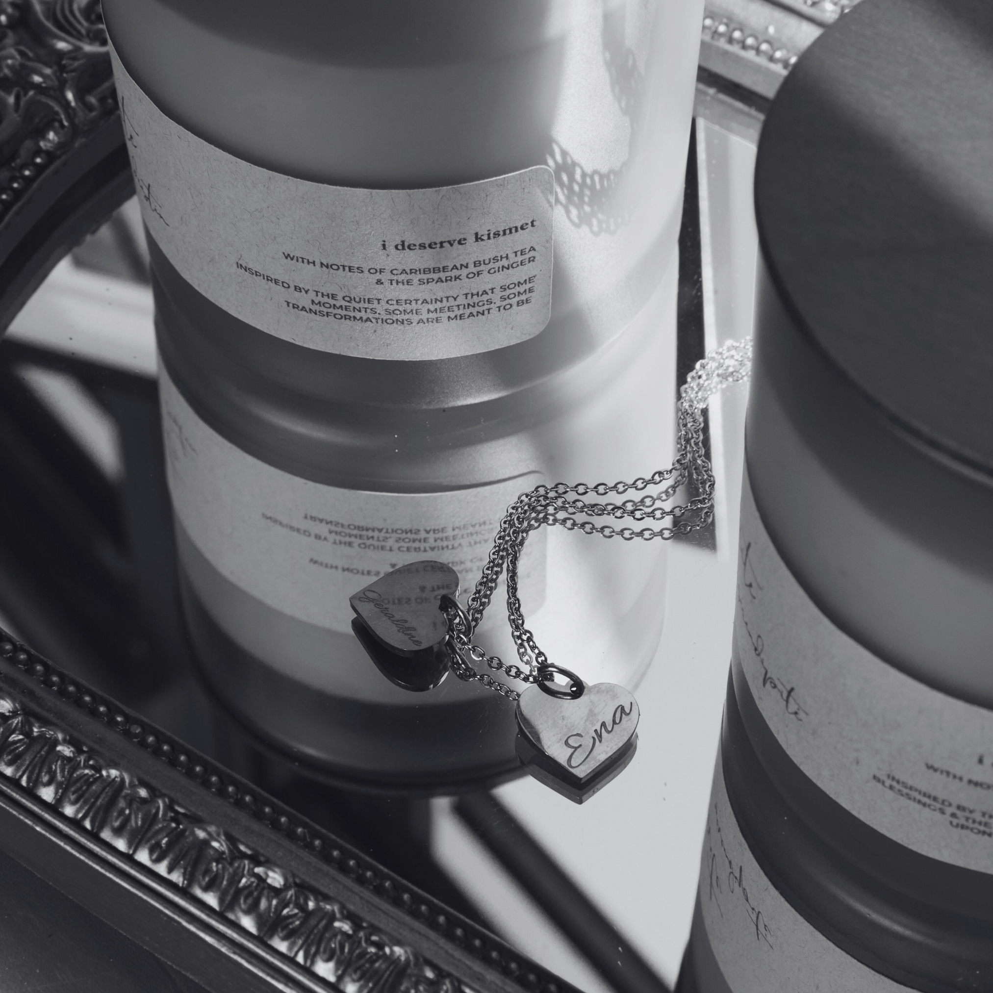 Two cylindrical containers with labels and a necklace on a reflective surface