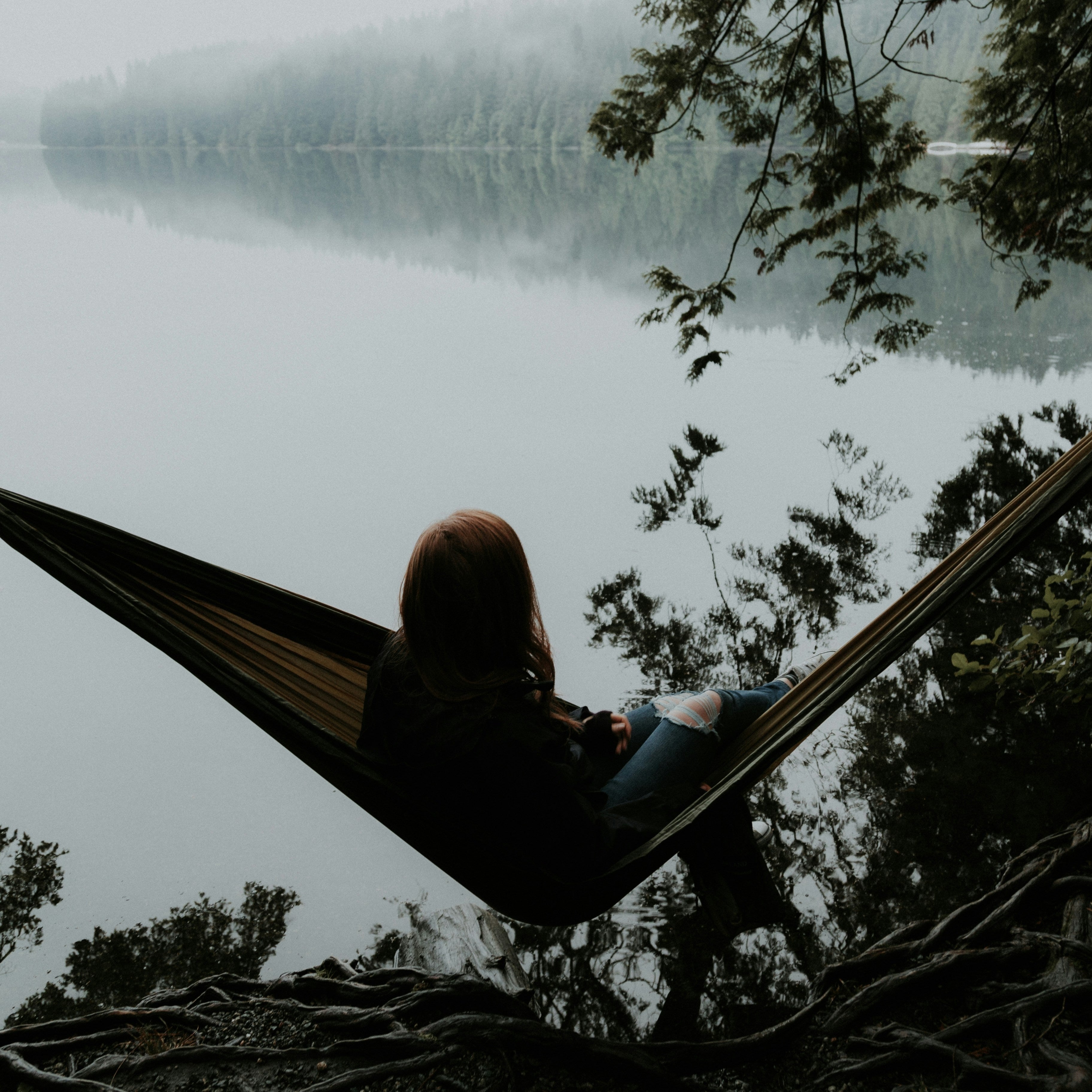 Person sitting in a hammock by a lake with trees in the background