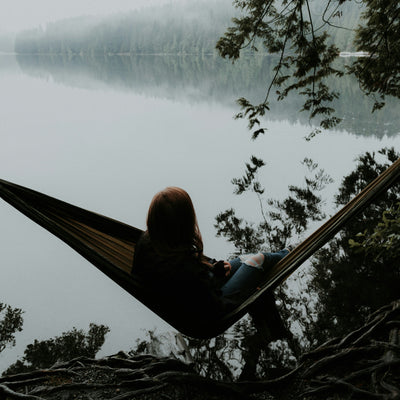 Person sitting in a hammock by a lake with trees in the background