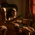 Woman sitting in a chair reading a book in a warmly lit room.