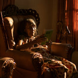 Woman sitting in a chair reading a book in a warmly lit room.