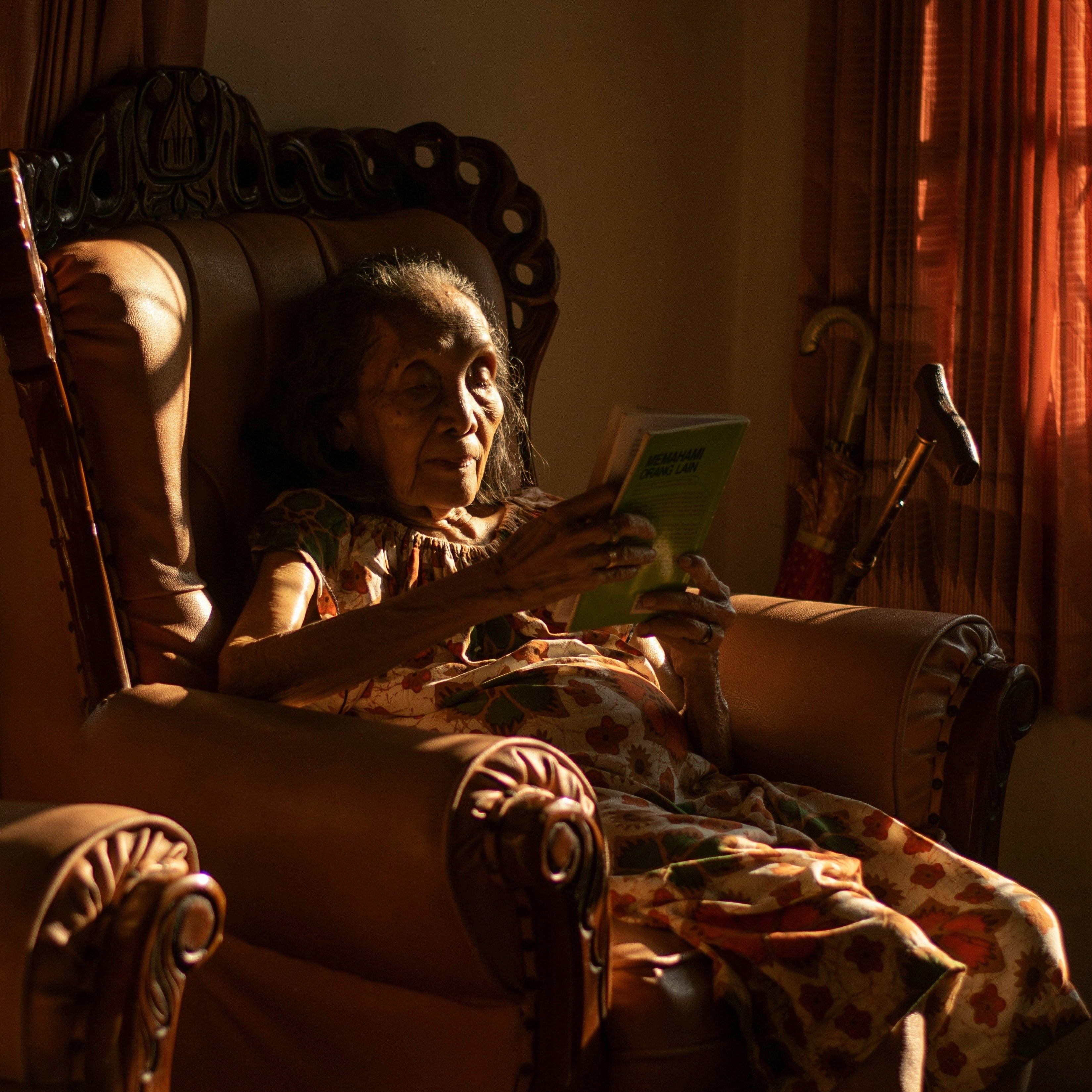Woman sitting in a chair reading a book in a warmly lit room.